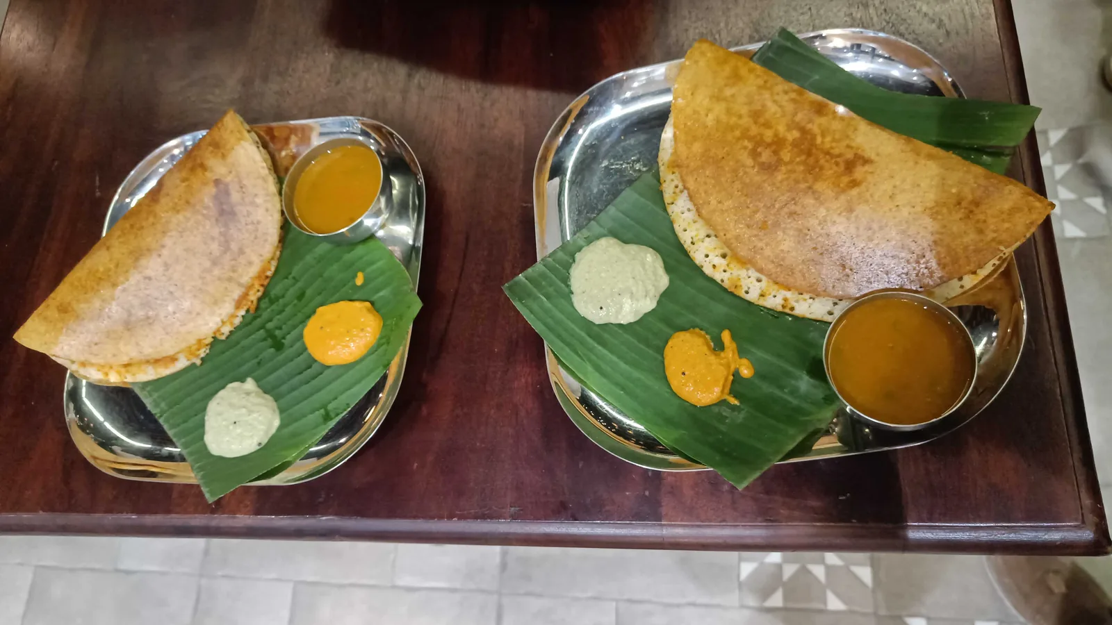 Two benne dosas at Madras Mandir Cafe in Jaipur, each on a steel plate over a banana leaf with coconut chutney, red chutney and a cup of sambar